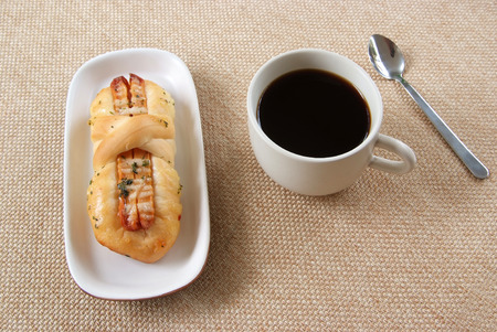 Appetizing sausage bread and cup of coffee on a fabric background 
