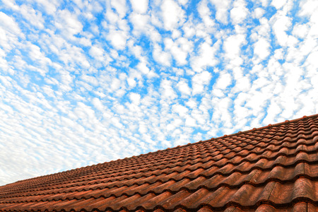 Red house roof and blue sky with white fluffy cloudsの写真素材