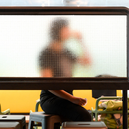 Woman is drinking coffee while sitting in modern coffee shop. Look through the mirror partition (silhouette)の写真素材