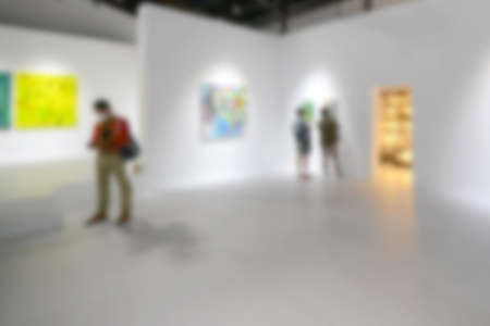 People looking at paintings on white wall in Art exhibition gallery. Blurry background.の写真素材