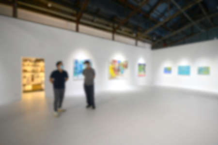 People looking at paintings on white wall in Art exhibition gallery. Blurry background.の写真素材