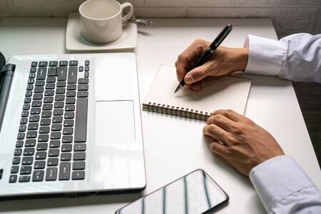 Businessman is taking a note on the notebook  from the financial imformation from laptop...