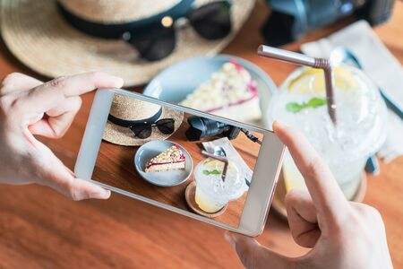 Close up of women's hands take a photo of cheese cake and drinks in cafe.の写真素材