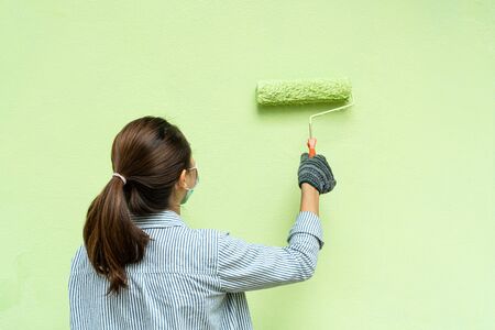 Back view of young women painter in blue and white striped shirt and gloves painting a wall with paint roller.の写真素材