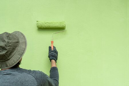 Back view of young men painter in T-shirt and gloves painting a wall with paint roller.の写真素材