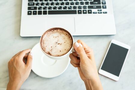 Women hold a cup of coffee  while looking at laptop in cafe.の写真素材