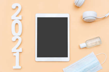 Flat lay of 2021 Goals with medical mask, sanitizer gel, headphone and tablet on beige color...