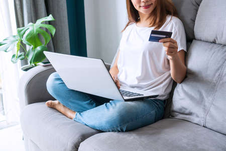 Happy young Asian woman holding credit card and using laptop computer. Businesswoman working at home office. Online shopping, e-commerce, internet banking, new normal conceptの写真素材
