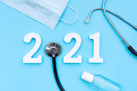 Flat lay of happy new year 2021. Number 2021 with stethoscope, medical mask and sanitizer gel on blue background. health medical and new normal lifestyle concept. Copy space, top viewの写真素材