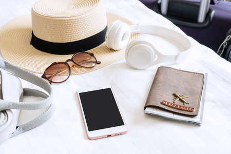 Summer hat, sunglasses, bag, headphone, passport and smartphone of woman traveler on bed in modern hotel room. Travel, relaxation, journey, trip and vacation concepts. Close up and copy space.の写真素材
