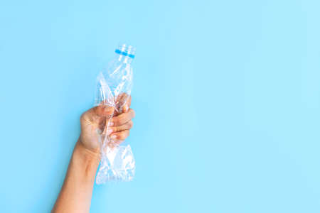 Hands crashing plastic bottles on blue background. Plastic utilisation concept. Ecological problem...