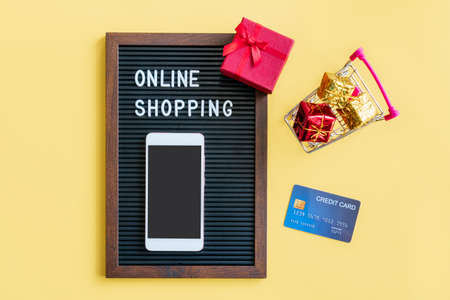 Miniature of gift boxes in trolley, smartphone, word on black frame and credit card on yellow...