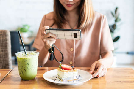 Beautiful Asian woman taking a photo of cake with smartphone before eating in cafeの写真素材