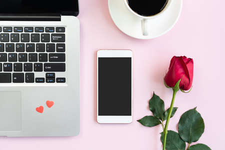 Rose, mobile phone, a cup of coffee and laptop on pink table background. Valentines day, anniversary, birthday concept. Flat lay, top view and copy space.の写真素材