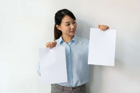 Asian businesswoman in blue shirt holds a blank sheet of paper in hands for advertisement isolated...