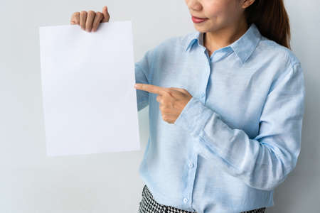 Beautiful young Asian woman in blue shirt holds a blank sheet of paper in hands for advertisement isolated over white background. Copy space.の写真素材