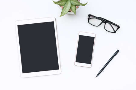 White office desk with tablet, smartphone, glasses and pen. Blank mobile phone and notepad for input...
