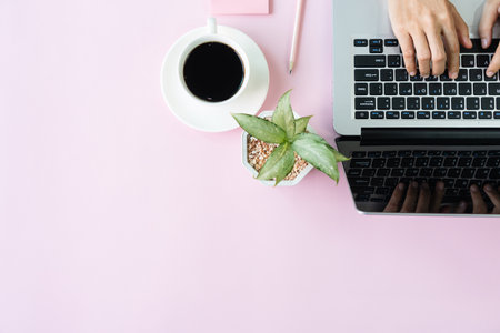 Woman hands using computer laptop wiith a cup of coffee and notepad on pink table. Business and technology, work from home concept. Top view and copy space.の写真素材