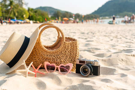 Straw hat, bag, sunglasses, coral and camera on sand at tropical beach. Summer holiday concept....