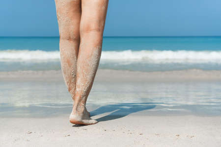 Young Asian woman walking on sand beach. Closeup detail of female feet and white sand. Beach, summer...