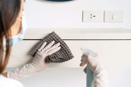 Housewife wearing a medical mask and hands in rubber protective glove with sanitizing spray bottle...