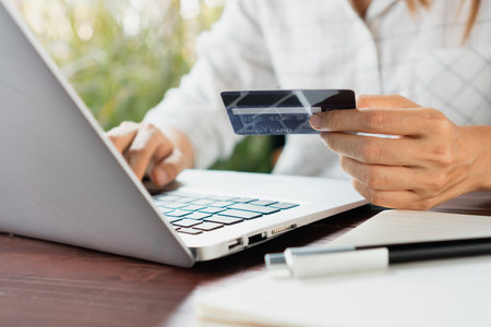 Closeup of Asian businesswoman typing on laptop keyboard while holding credit card, Women shopping online or booking a ticket on notebook. Business, technology and lifestyle concept.の写真素材