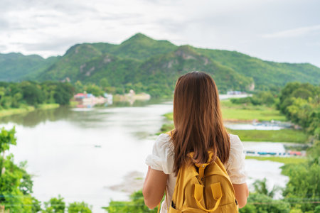 Happy traveler Asian woman with yellow backpack enjoy at river and mountain view on vacation. travel concept.の写真素材
