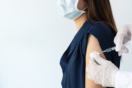 Hands of doctor or nurse holding syringe making covid 19 vaccination injection dose in shoulder of female patient. Flu influenza vaccine clinical trials concept. Closeup, copy spaceの写真素材