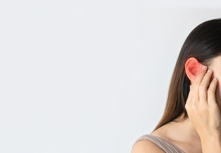 Young Asian woman has a sore ear, suffering from otitis over white background with red accent, free space, closeupの写真素材