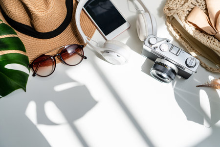 Flat lay of summer accessories with green tropical leaf shadow on white desk. Summer, holiday and...