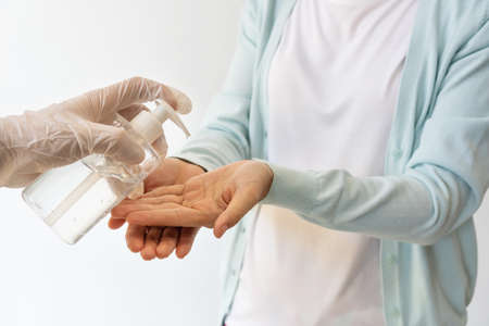 Hand in glove apply alcohol antiseptic gel on to woman hands to protect against infection of  pandemic.Young girl washing hands with hand sanitizer gel. Health care concept.の写真素材