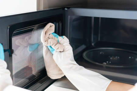 Woman hand with microfiber rag cleaning inside of microwave oven in kitchen at home. Closeupの写真素材