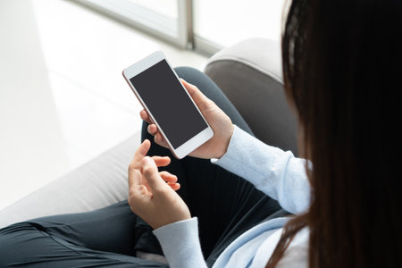 Woman hands using mobile phone while sitting on sofa in living room at home. Business, technology...