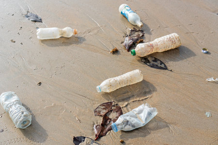Spilled plastic garbage abandoned on the beach of the big city. Empty used dirty bottles on sand....