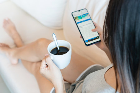 Attractive young Asian woman relaxing on sofa at home in the morning while have some coffee and using smartphone. Technology and lifestyle concept. Top viewの写真素材