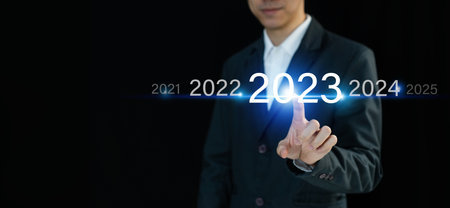 Businessman finger pressing and pointing on year 2023 on virtual screen on dark background with copy space. Business planning, goals and achievement in 2023. Happy new year conceptの写真素材