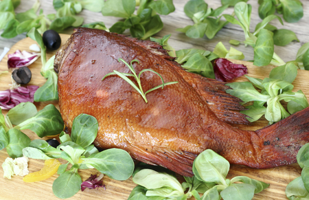 Smoked sea bass on an old wooden table with corn salad leaves. の写真素材