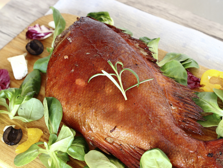 Smoked sea bass on an old wooden table with corn salad leavesの写真素材