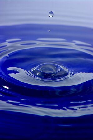 A high speed shot of a droplet of water, before it hits the blue liquid surface.の写真素材
