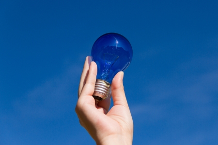 Hand holds a light bulb and a blue skyの写真素材