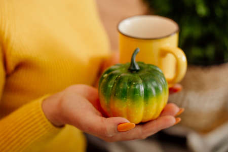 girl in a yellow sweater holds a cup and a decorative pumpkinの写真素材