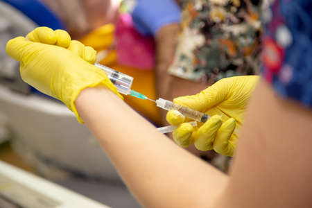 Doctor in yellow gloves holding syringes in preparation for injectionの写真素材