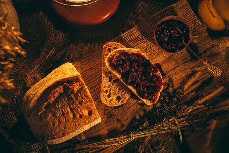 Sliced ââbread with jam in the light of candles on a wooden board. Rustic atmosphere.Photo from the topの写真素材