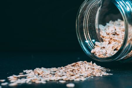 A scattering of oatmeal with a jar on a dark backgroundの写真素材