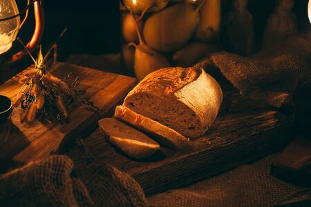 Pieces of sliced ââfreshly baked bread in the light of candles. Bread on a wooden board.Rural cozy surroundingsの写真素材
