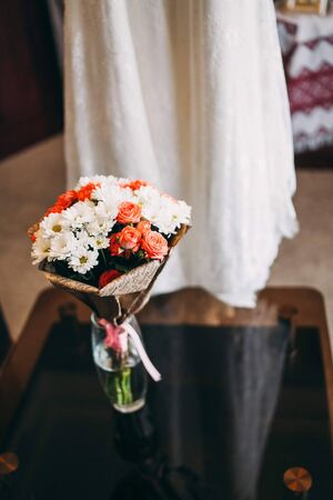 Bouquet of pink roses and white asters standing in a vase on a black glass table on the background of which a wedding dressの写真素材