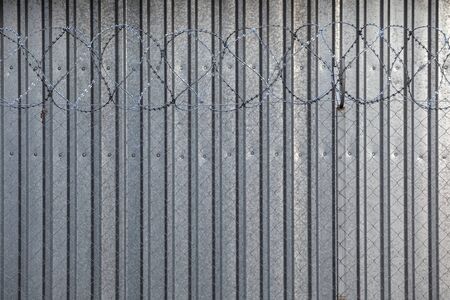 Barbed wire on the background of a tin tin fence. High metal fenceの写真素材