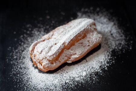 Photo of eclair with cream from the top on a black background. Eclair in powdered sugarの写真素材