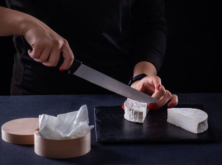 Girl slices goat brie cheese on a dark background.の写真素材