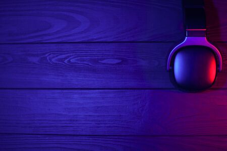 Headphones on  black  wooden background. Red-blue neon light.Stylish wireless headset in neon...